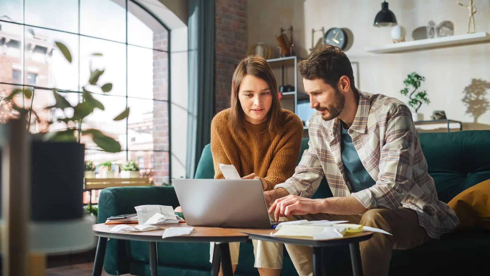 A couple sitting in a cozy living room, reviewing receipts and working on a laptop, possibly managing finances or taxes
